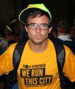 camp: Caleb Dufresne (headshot), program director for Live Oak Wilderness Camp, serious-looking man with arms outspread wearing green ball cap, glasses, orange T-shirt that says We Built This City, backpack