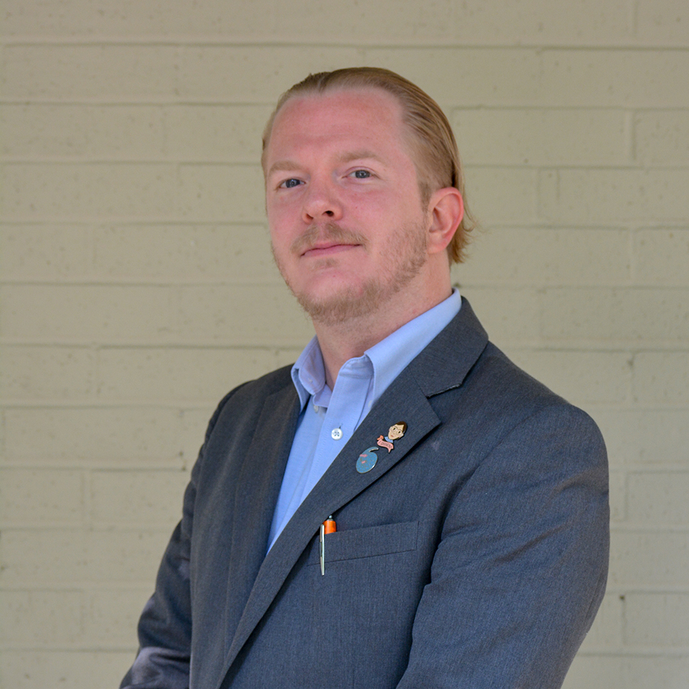 professional development plan: Justin Hensley (headshot), program manager at After-School All-Stars North Texas, man with widow’s peak, reddish beard, mustache, blue suit jacket with 2 lapel pins, light blue button-down shirt