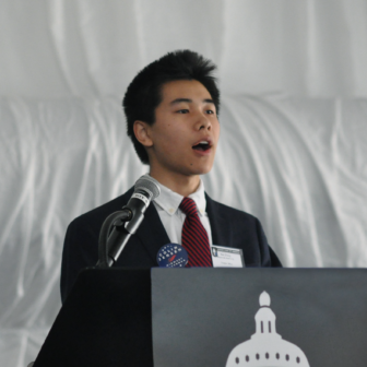 JSA: Max Zhang (headshot), chair of JSA’s student-run Council of Governors, young man in dark suit, white shirt, red striped tie speaking at podium