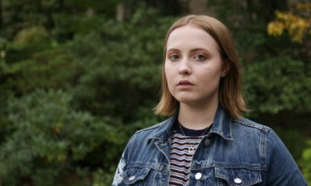 TAG: Young woman in jean jacket, striped top, necklace stares into camera