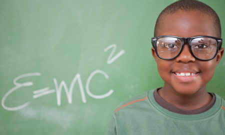 inventors: smiling little boy in green T-shirt with huge glasses in front of blackboard with E=mc²
