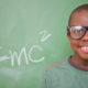 inventors: smiling little boy in green T-shirt with huge glasses in front of blackboard with E=mc²