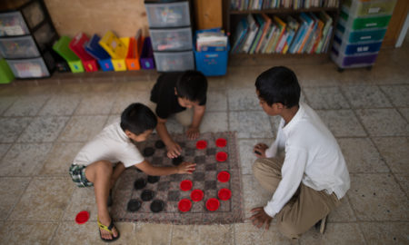 Afterschool: Children playing checkers on mat checkerboard on the floor.