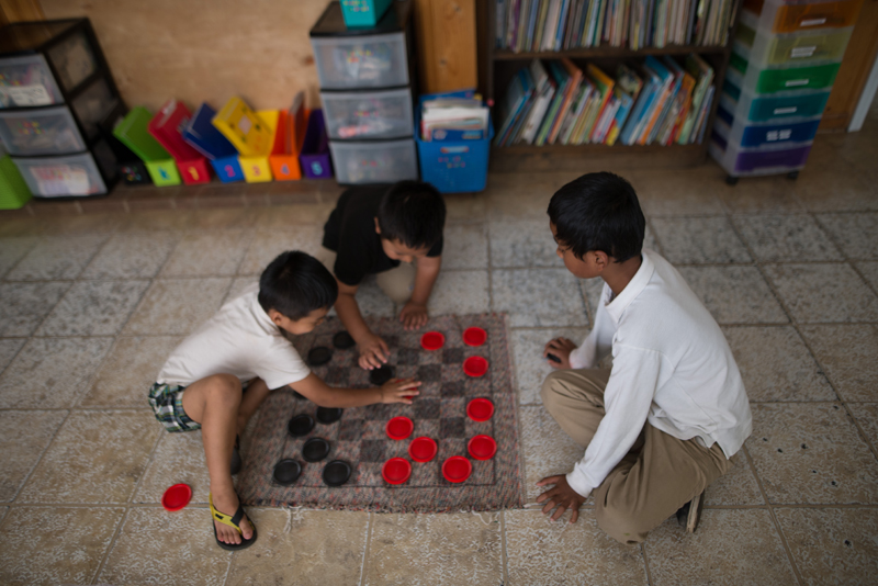 Afterschool: Children playing checkers on mat checkerboard on the floor.