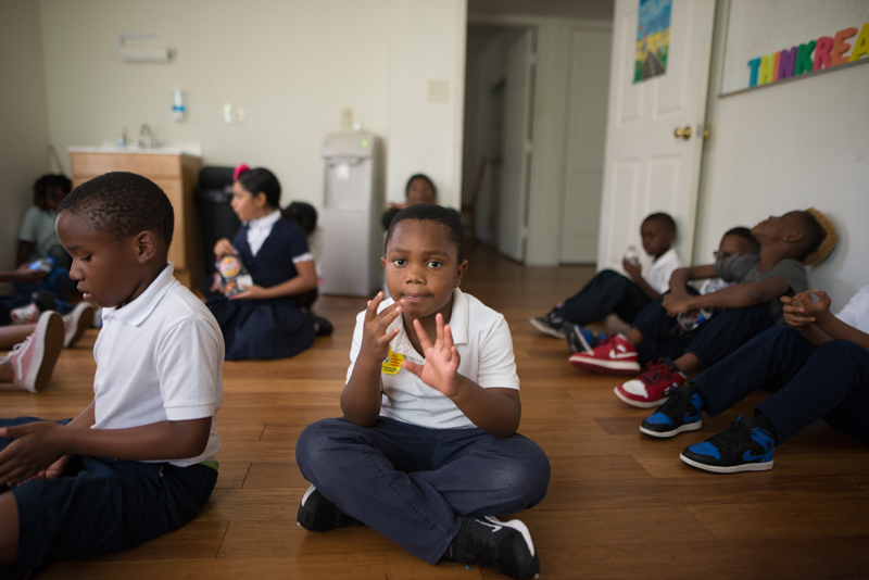 afterschool: Little girl in white polo shirt, jeans sits on floor, surrounded by other kids.