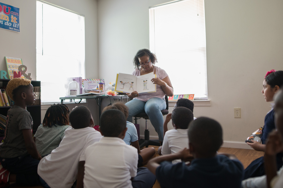 afterschool: Woman reads picture book to children sitting on the floor.