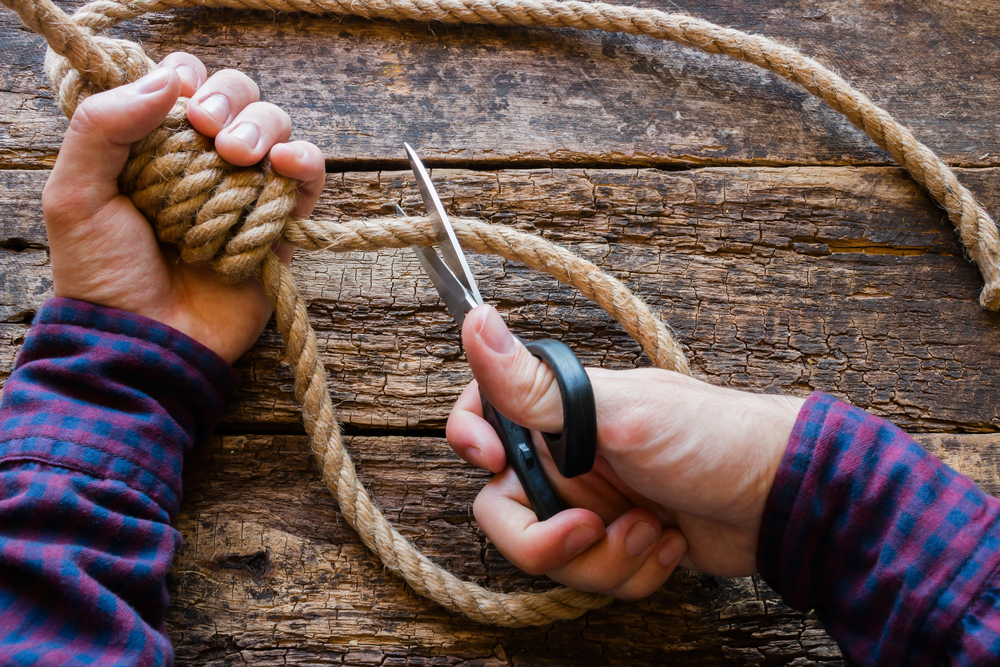 suicide prevention: hands cutting slipknot of rope with scissors
