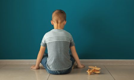 Autism prevalence report; young boy sitting facing wall with toy plane
