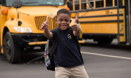 afterschool: Smiling little boy with missing front teeth gives two thumbs up in front of school buses.