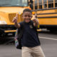 afterschool: Smiling little boy with missing front teeth gives two thumbs up in front of school buses.