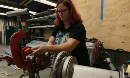foster care: Woman with red hair, glasses, T-shirt works with machinery.
