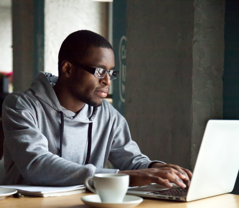 disconnected youth: Serious millennial African-American man using laptop sitting at cafe table