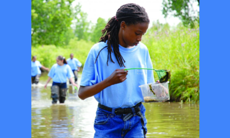 youth environmental stem education grants; young girl wading in stream studying nature