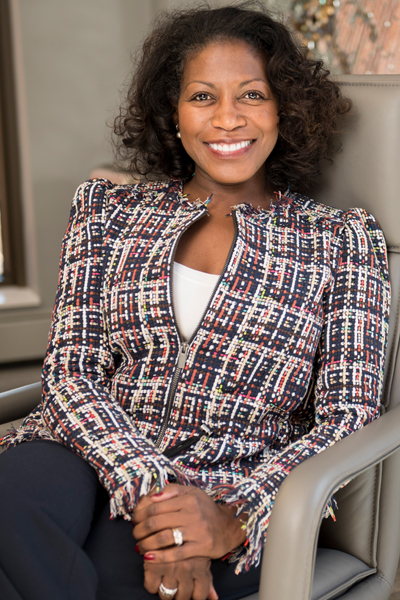Casey: Smiling woman with curly dark hair wearing zippered print jacket sitting in executive office chair.
