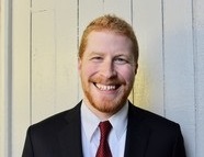 gun violence: Smiling red-headed man in dark suit, white shirt, tie.