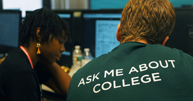 College Possible: Young woman with earrings sits next to man wearing T-shirt with Ask Me About College on back.