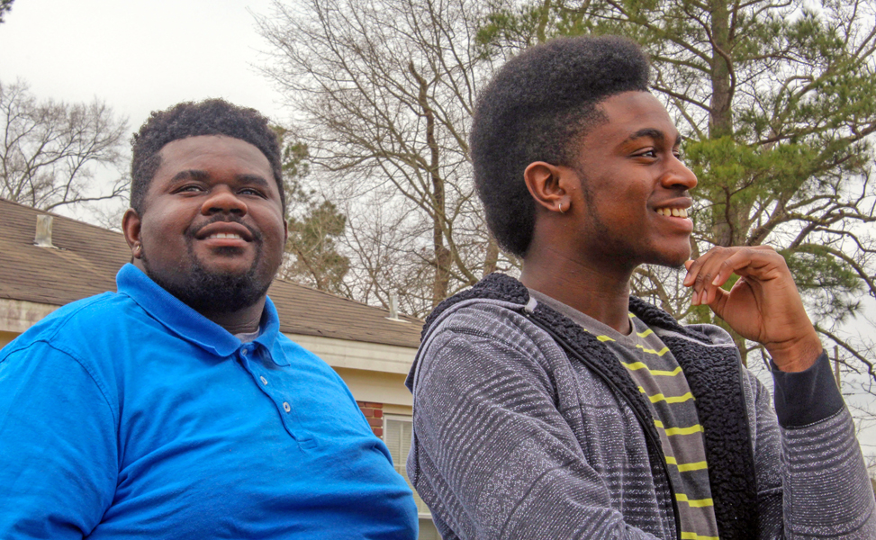 foster care: Young man in blue shirt looks ahead; young man on right with earring in striped sweater looks to right.