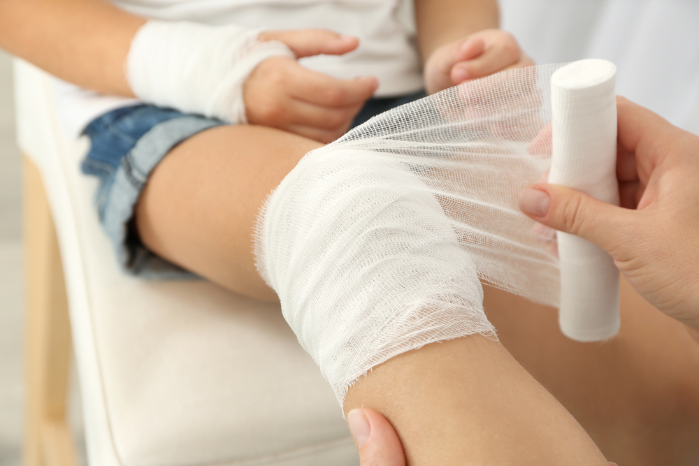 camp: Woman winding bandage around little girl's knee.