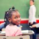 $23 billion education racial disparity report; young black girl in classroom looking back at camera