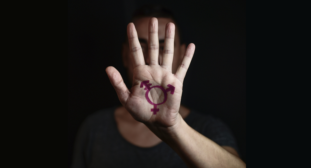 transgender youth, high school youth report; young man holding hand to camera with transgender symbol on it