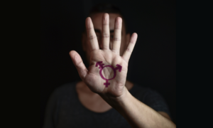 transgender youth, high school youth report; young man holding hand to camera with transgender symbol on it