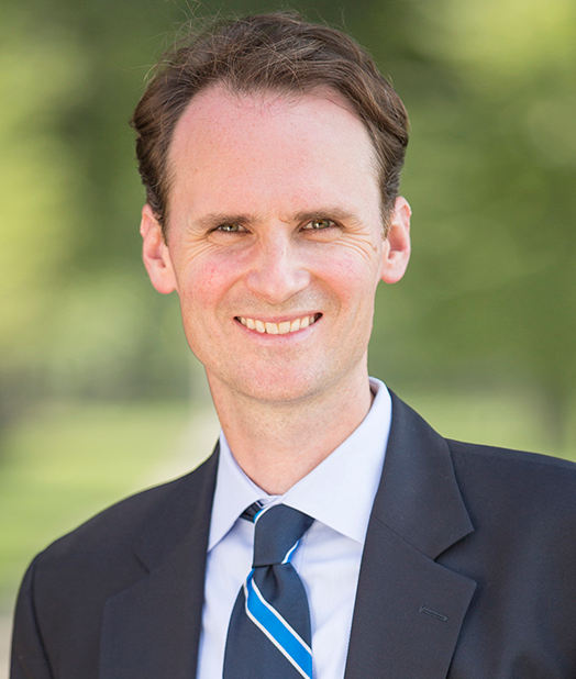 John Palfrey newsmaker headshot; man standing in front of natural background in suit