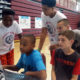 STEM: Kids in T-shirts, shorts cluster around computer on basketball court.