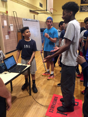 STEM: Students around a laptop on basketball court argue as one stands on mat connected to laptop.