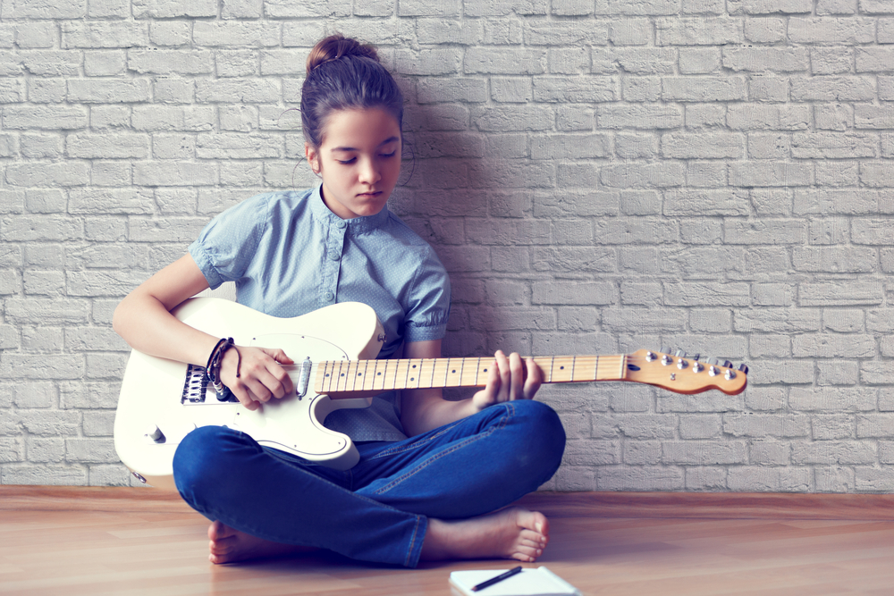 afterschool: Young girl plays guitar and composes music on a background of a brick wall.