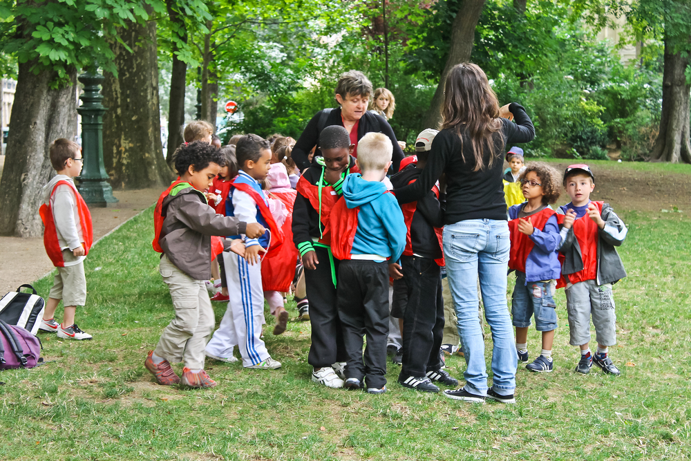 Group of unidentified kids with two teachers in the city park. 