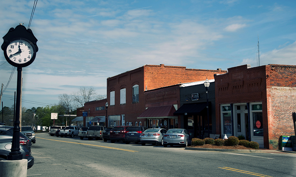 rural: Row of 1- and 2-story storefronts with cars parked diagonally in front of them.