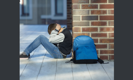 school violence prevention grants; young student sitting on ground at school covering head