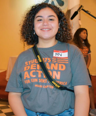 MariaVictoria Chacón-Briceño, chapter lead of Students Demand Action Miami, smiling young woman with brown curly hair, T-shirt that says students demand action.