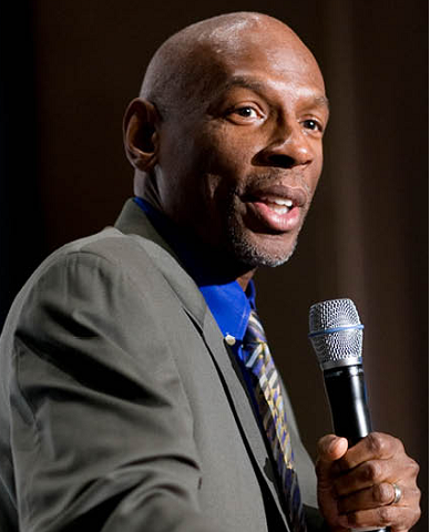 Geoffrey Canada newsmaker headshot, African American bald man in suit with microphone
