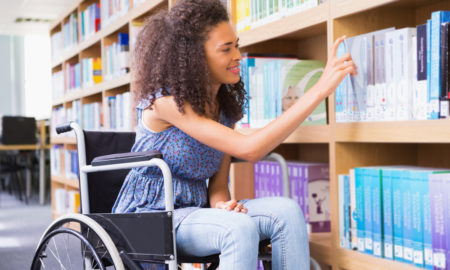 disability: student in wheelchair in library picking book at the university