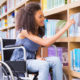 disability: student in wheelchair in library picking book at the university