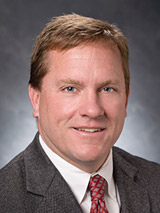 David Meyers (headshot), teaches at JW Fanning Institute for Leadership Development, smiling man with short brown hair, gray jacket, white shirt, patterned red tie.