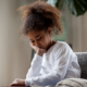 toxic stress and children's outcomes report; troubled african american girl sad on couch