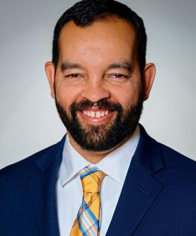 Dennis Quirin newsmaker headshot; smiling, bearded man in suit and tie