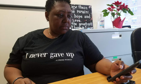 Woman in T-shirt that says I never gave up sits at table, looks at her phone.