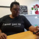 Woman in T-shirt that says I never gave up sits at table, looks at her phone.