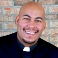 South: Smiling bald man with short beard, mustache wearing clerical collar.
