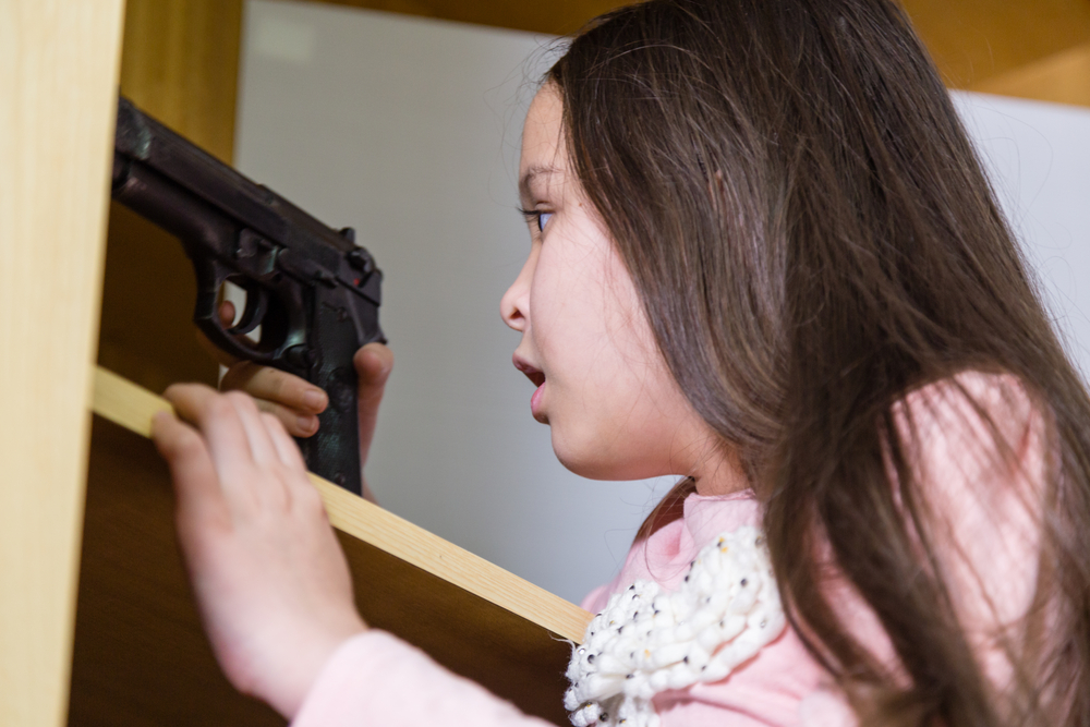 gun safety: Young child finds pistol in cupboard, gun control concept 