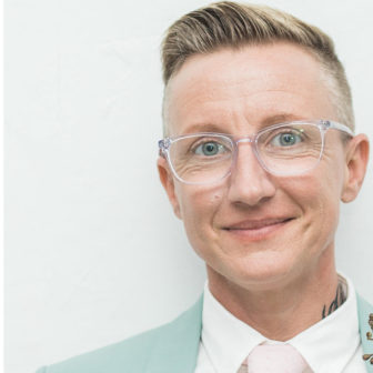 LGBTQ : Jama Shelton (headshot), assistant professor at Silberman School of Social Work, smiling person with short blond hair, glasses, light green jacket, white shirt, pale pink tie 