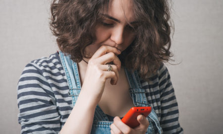 gun violence: Young woman looking at phone with concern, worry.