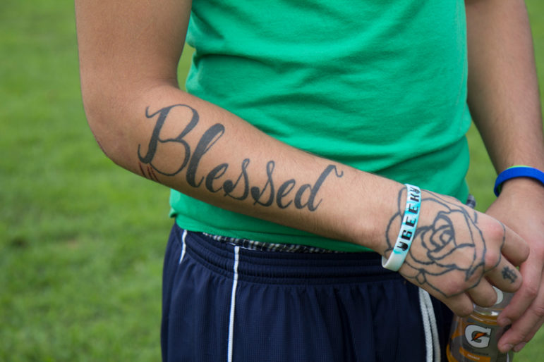 dog training: Tattoo of word blessed and flower image on right arm of someone in green shirt, blue athletic pants.