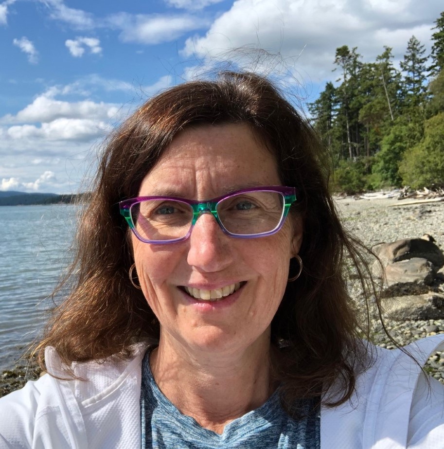coach: Yvonne Unrau (headshot), director of Center for Fostering Success at Western Michigan University, smiling woman with brown hair, multicolored glasses, white jacket at beach