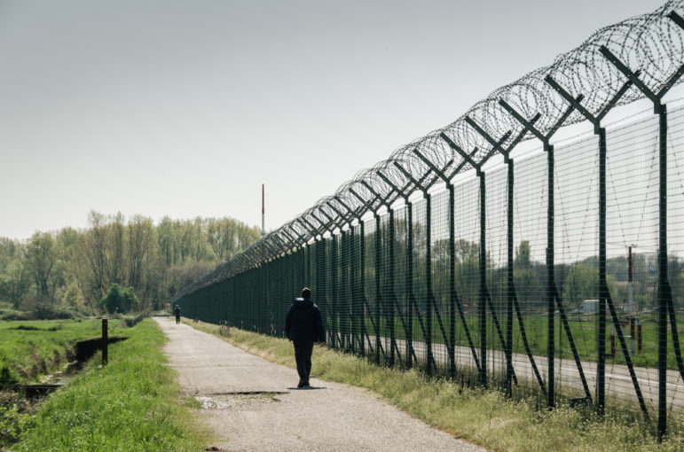 criminal record: Silhouette of man walking along a barbed wire high fence