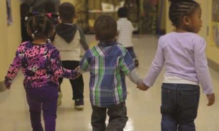 Young children holding hands walking in school hallway.