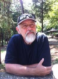 disposable: Hans Skott-Myhre (headshot), professor in Social Work and Human Services Department at Kennesaw State University, serious-looking man with gray mustache, beard, wearing dark T-shirt, ball cap with sunglasses on bill, outside near trees.